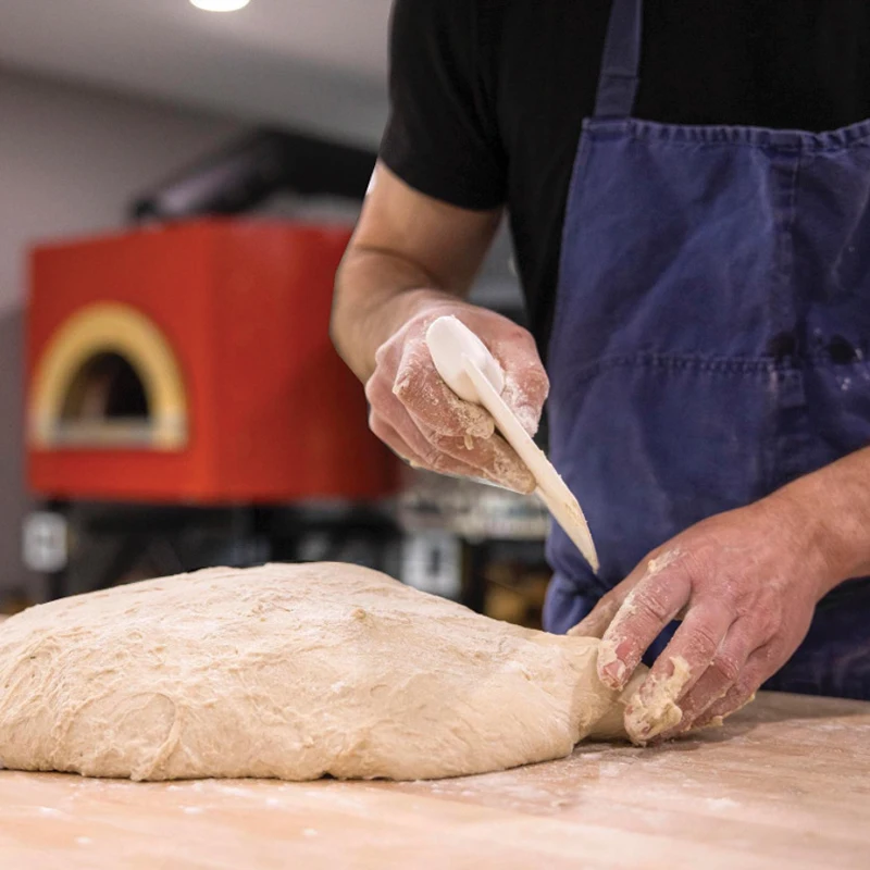 Panettiere taglia impasto per pane con forno Pavesi in sfondo